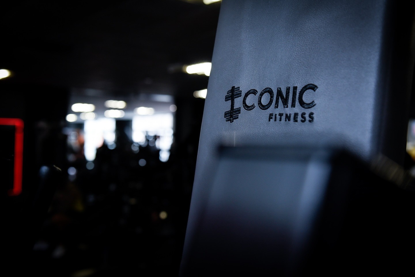 Machine pad embossed with the Iconic Fitness barbell logo, gym lights blurred behind